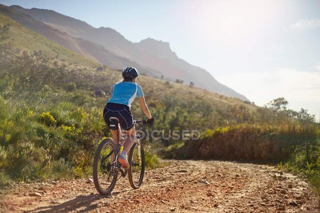 Молодая женщина катается на горном велосипеде по солнечной, удаленной грунтовой дороге — стоковое фото
