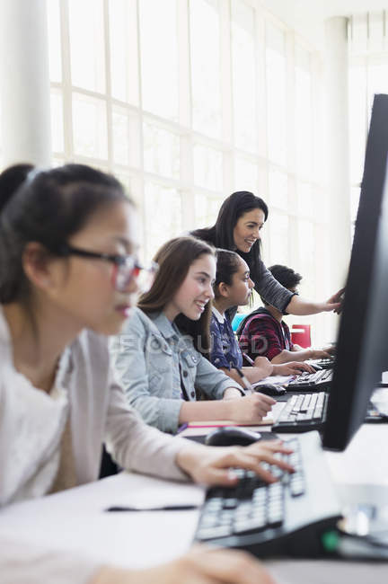 Enseignante aidant les élèves travaillant dans des ordinateurs en salle de classe informatique — Photo de stock