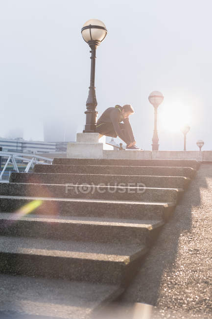 Мужчина бегун завязывает обувь на солнечном городском фонарном столбе — стоковое фото