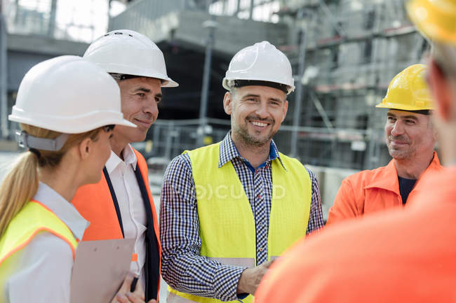 Smiling engineers and construction workers meeting at construction site — Stock Photo
