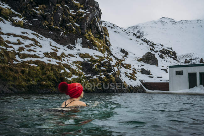 Frau mit Strumpfmütze schwimmt unter schneebedeckten Bergen, Island — Stockfoto