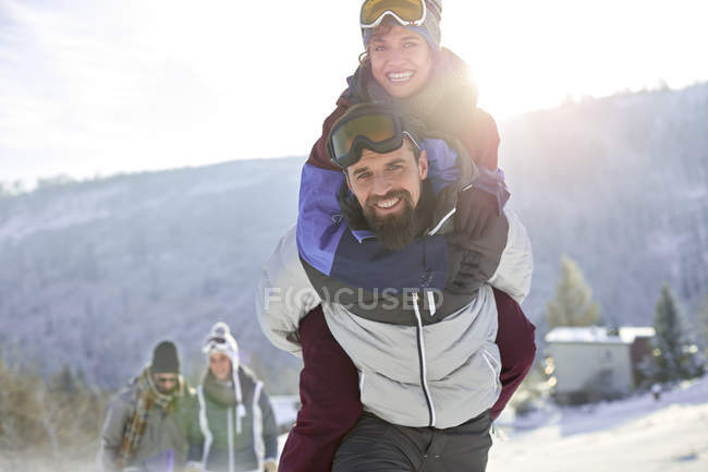 Portrait playful couple piggybacking in sunny, snowy field — Stock Photo