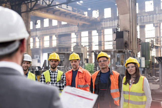 Steel workers listening to manager in meeting in factory — Stock Photo