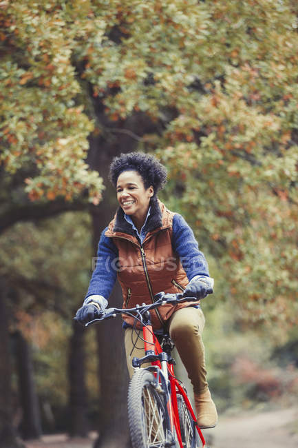 Улыбающаяся женщина катается на велосипеде в осеннем парке — стоковое фото