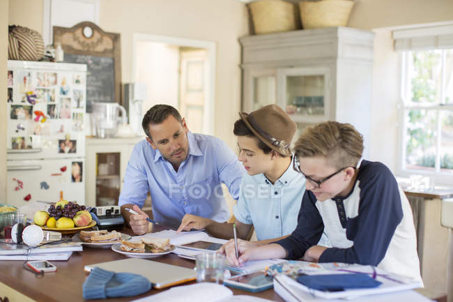 Hombre adulto medio ayudando a chicos adolescentes con su tarea en la mesa - foto de stock