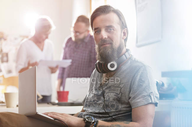 Портрет улыбающийся мужчина дизайнер с наушниками с помощью ноутбука в офисе — стоковое фото
