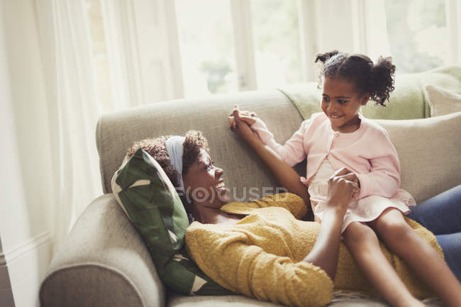 Playful mother and daughter holding hands on sofa — Stock Photo