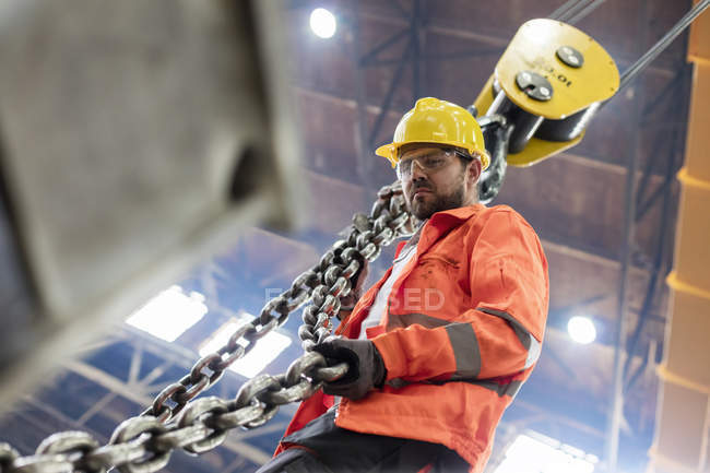 Trabajador de acero que sostiene la cadena de grúa en fábrica - foto de stock