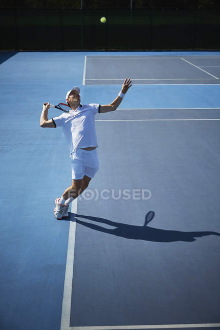 Jovem jogador de tênis masculino jogando tênis, servindo a bola no campo de tênis azul ensolarado — Fotografia de Stock