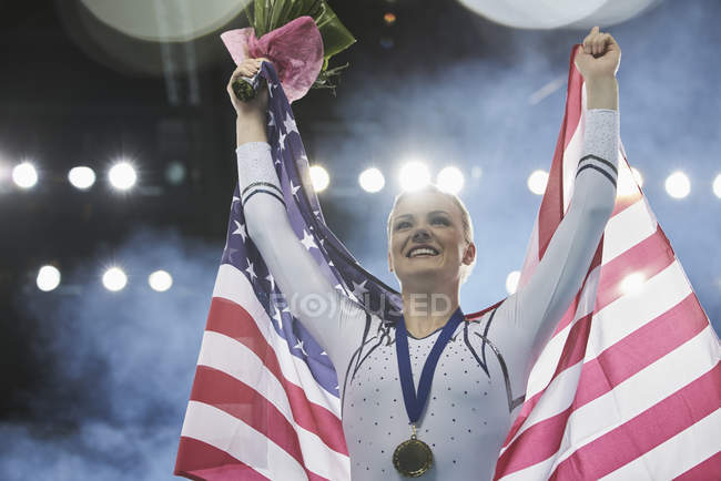 Femme gymnaste souriante célébrant la victoire tenant le drapeau américain — Photo de stock