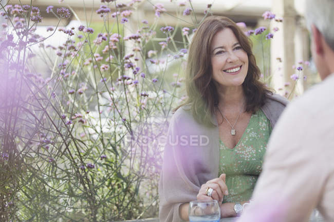 Pareja madura sonriente hablando en el patio con flores moradas - foto de stock