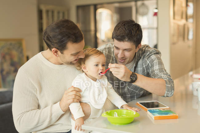 Чоловічі гей-батьки годують дитину сином на кухні — стокове фото