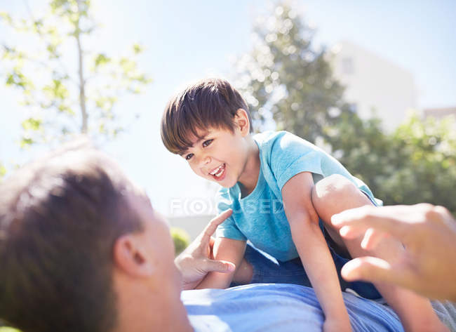 Син сміється, лежачи на вершині батька на сонячному патіо — стокове фото