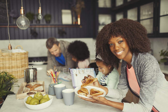 Портрет улыбающейся матери, завтракающей тостами с молодой семьей на кухне — стоковое фото