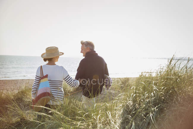 Ältere Paare gehen Arm in Arm am sonnigen Strand — Stockfoto