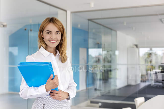 Retrato sonriente mujer de negocios sosteniendo carpetas en la sala de conferencias - foto de stock