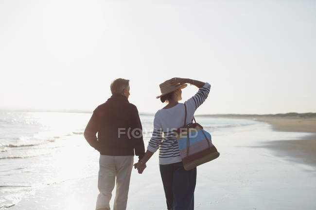 Liebevolles reifes Paar hält Händchen und geht am sonnigen Strand spazieren — Stockfoto