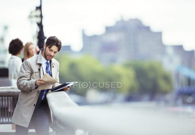Homme d'affaires lisant un journal sur le front de mer urbain — Photo de stock