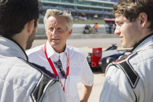 Manager talking to formula one drivers on sports track — Stock Photo