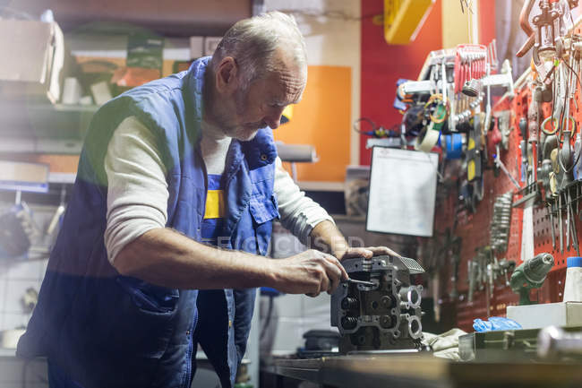 Senior mâle mécanicien de moto fixation partie moteur dans l'atelier — Photo de stock