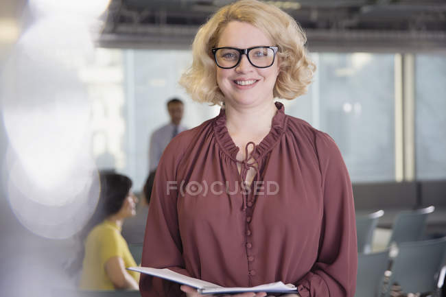 Portrait femme d'affaires souriante et confiante avec paperasserie au bureau — Photo de stock