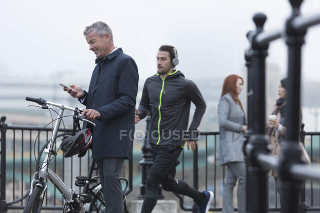 Бизнесмен с велосипедным текстом с сотовым телефоном и бегун на городской рампе — стоковое фото