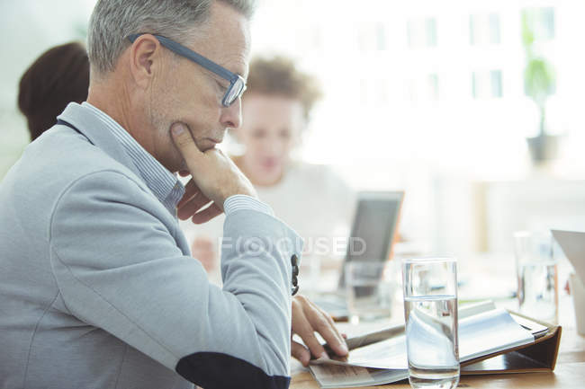 Portrait of businessman sitting at table in conference room and reading newspaper — Stock Photo