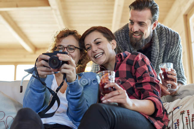 Друзья смотрят на фотографии на цифровой камере и пьют горячий тодди в хижине — стоковое фото