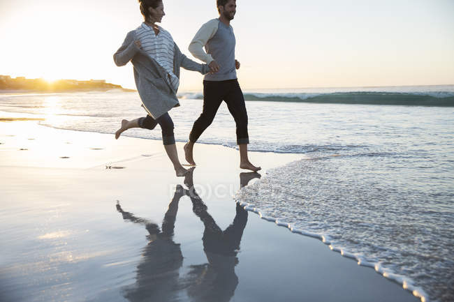 Young couple holding hands and running on beach — Stock Photo