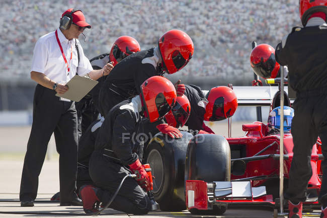 Manager with stopwatch timing pit crew replacing formula one race car tire in pit lane — Stock Photo
