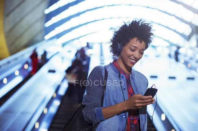 Smiling woman listening to mp3 player on escalator — Stock Photo