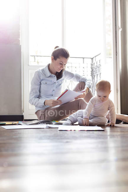 Baby-Tochter spielt auf dem Boden neben arbeitender Mutter — Stockfoto