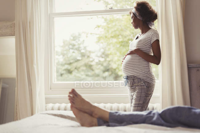 Pensive pregnant woman looking out bedroom window — Stock Photo