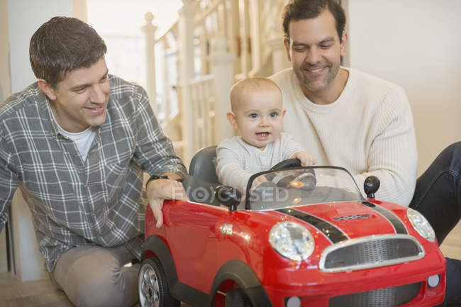 Macho gay padres y bebé hijo jugando con juguete coche - foto de stock