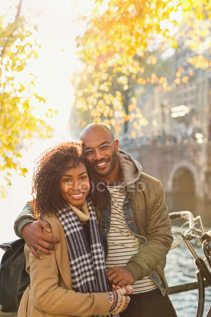 Retrato sorrindo, casal afetuoso abraçando ao longo do canal de outono ensolarado — Fotografia de Stock