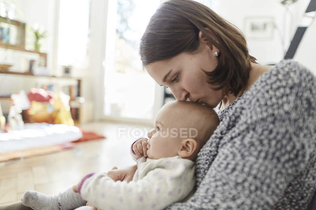 Madre besando bebé hija en la cabeza - foto de stock