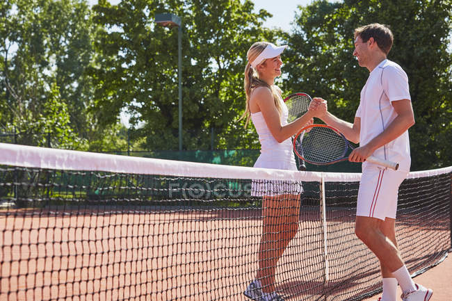 Male and female tennis players fist bumping at net on sunny clay tennis court — Stock Photo