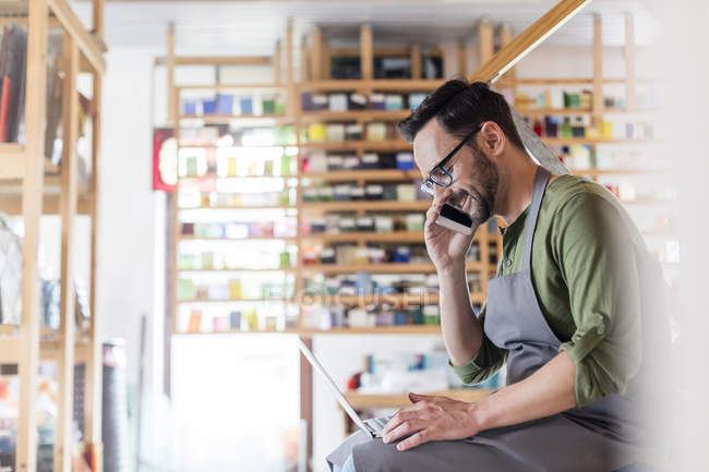 Artista de vidro manchado falando no telefone celular e usando laptop em estúdio — Fotografia de Stock