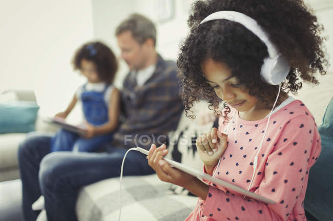 Chica con auriculares usando tableta digital en el sofá - foto de stock