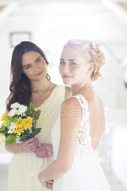 Retrato de novia y dama de honor con ramo de flores en habitación doméstica - foto de stock