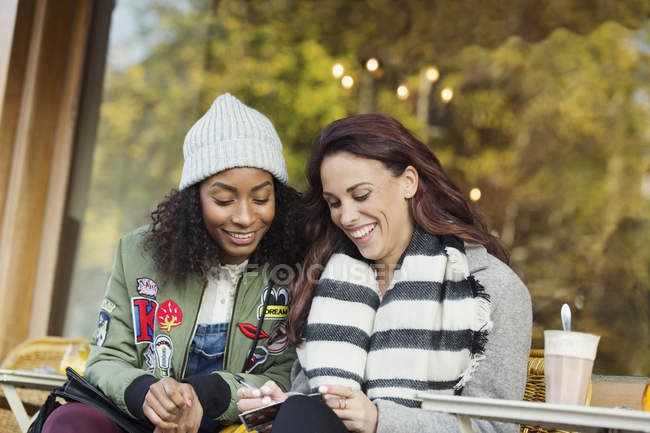 Smiling young women friends writing postcard at urban sidewalk cafe — Stock Photo