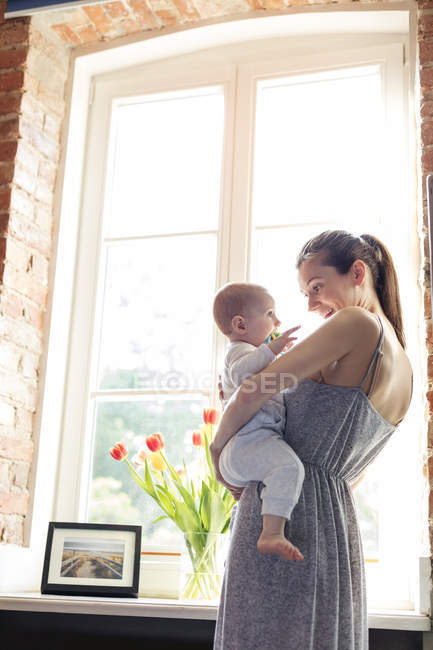 Mãe segurando bebê filha na janela — Fotografia de Stock