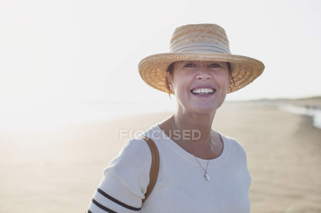 Портрет улыбающейся зрелой женщины в соломенной шляпе на солнечном пляже — стоковое фото