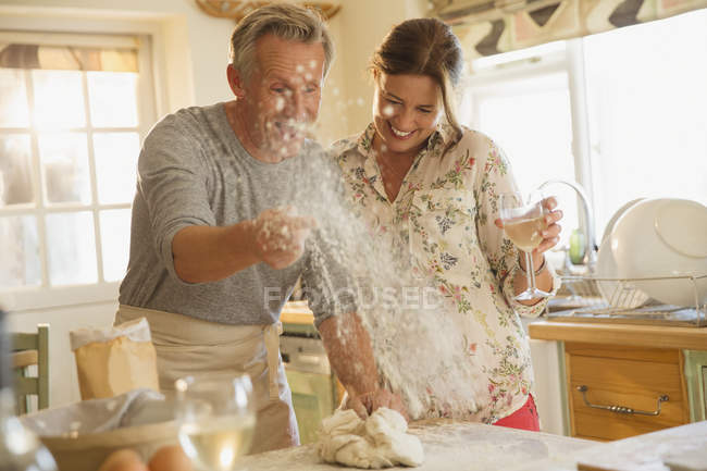 Brincalhão casal maduro assar, jogando farinha e beber vinho na cozinha — Fotografia de Stock