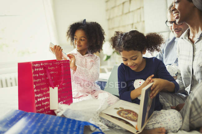 Genitori che guardano le figlie aprire il regalo di compleanno sul letto — Foto stock