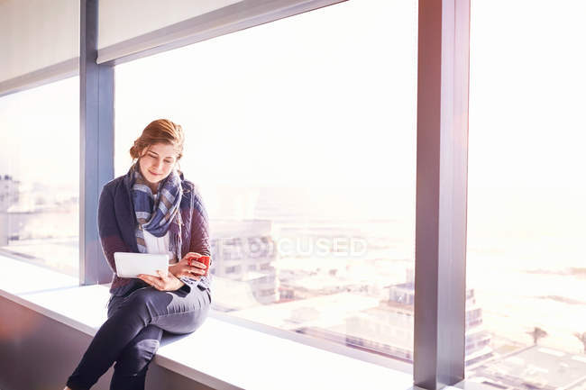 Бізнес-леді за допомогою цифровий планшет і пити каву в Сонячний Міський офіс вікно — стокове фото