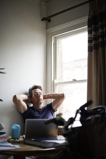 Чоловік сидить за столом з відкритим ноутбуком, розслабляючим — стокове фото