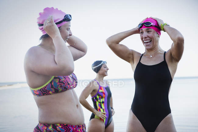 Lächelnde Freiwasserschwimmerinnen passen Badekappen am Meer an — Stockfoto