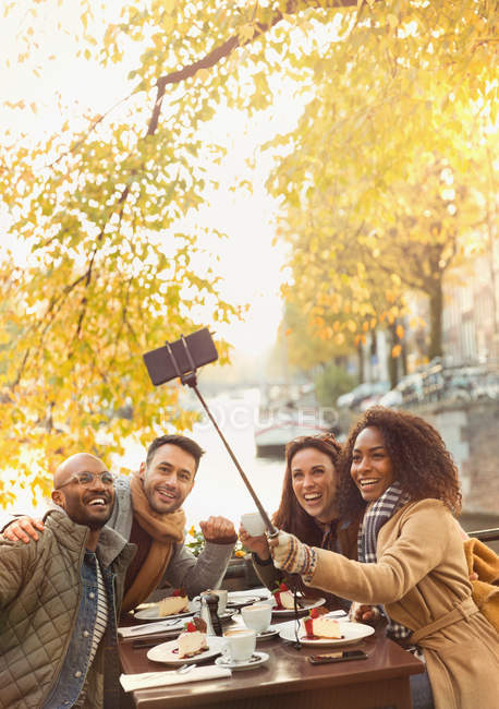 Amici sorridenti scattare selfie con bastone selfie al caffè marciapiede autunno — Foto stock