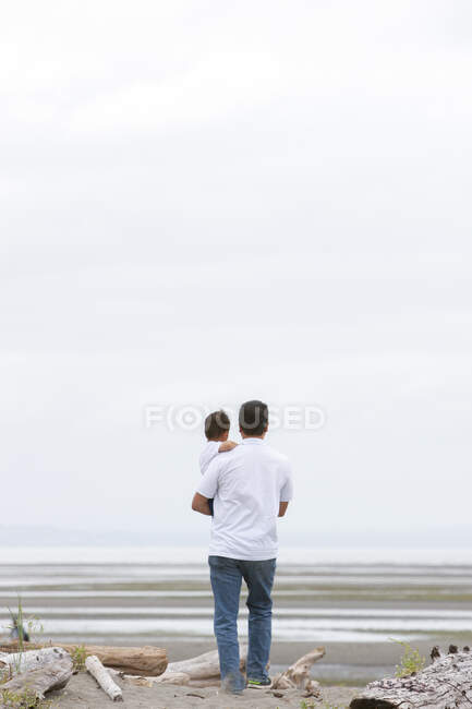 Pai segurando na praia nublada — Fotografia de Stock